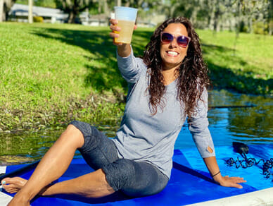 Woman holding up a mimosa seated on paddleboard.
